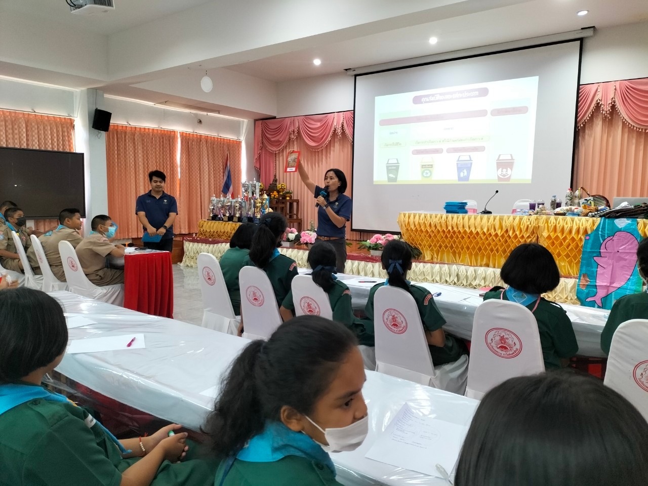 A group of people sitting in chairs and a person standing in front of a projector screen

AI-generated content may be incorrect.